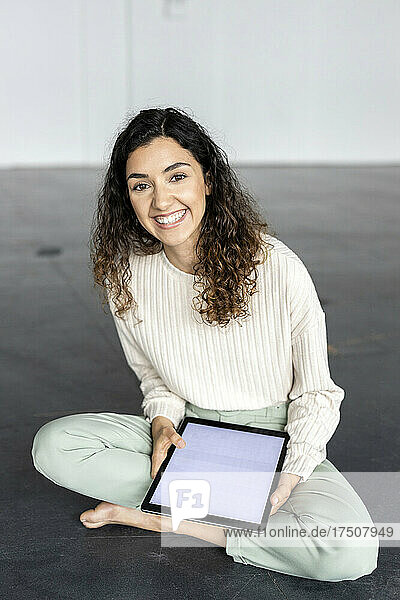 Smiling businesswoman sitting cross-legged and holding tablet pc on floor