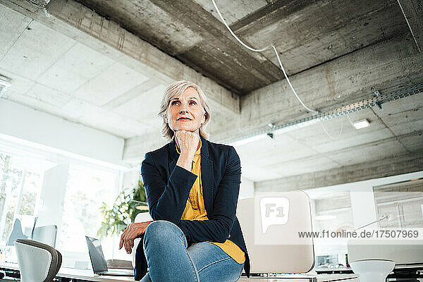 Businesswoman with hand on chin sitting on desk