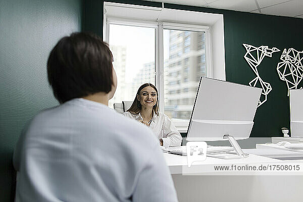 Lächelnde Verkäuferin spricht mit Kunden am Schreibtisch im Reisebüro