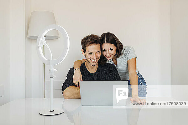 Smiling young couple using laptop together on table at home