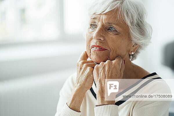 Thoughtful woman with hands on chin at home