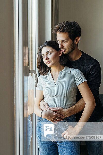 Young couple looking through window at home