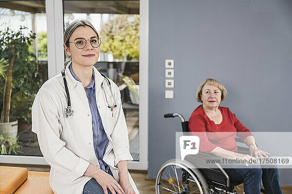 Smiling doctor sitting with disabled woman in background at home