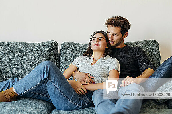 Lächelndes junges Paar  das beim gemeinsamen Sitzen auf dem Sofa nachdenkt