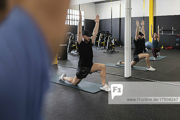 Trainer mit erhobenen Armen unterstützt Sportler beim Training im Fitnessstudio