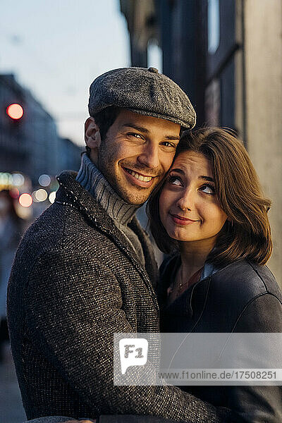 Smiling girlfriend looking at boyfriend wearing hat in city