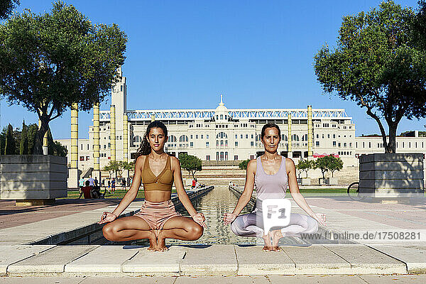 Teenage girl doing yoga with mother by water basin