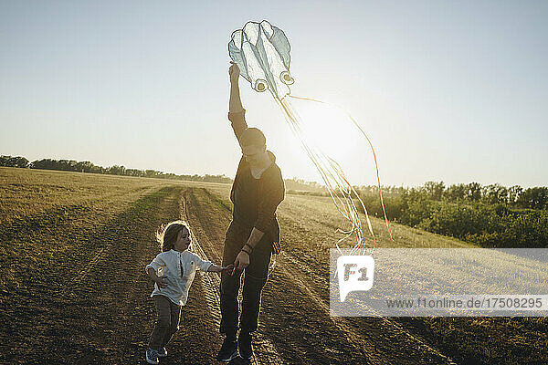 Daughter playing with father holding kite on dirt road