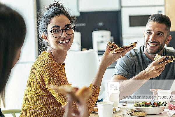 Smiling colleagues with pizza looking at businesswoman in office