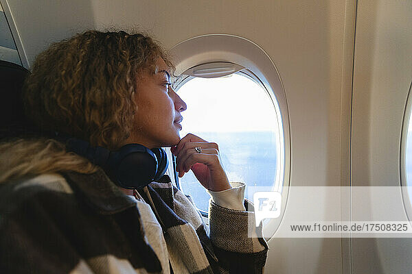 Junge Frau mit der Hand am Kinn schaut aus dem Flugzeugfenster