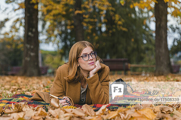 Young woman with hand on chin contemplating in autumn park