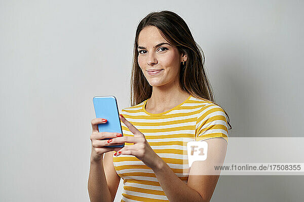 Young woman holding mobile against gray background