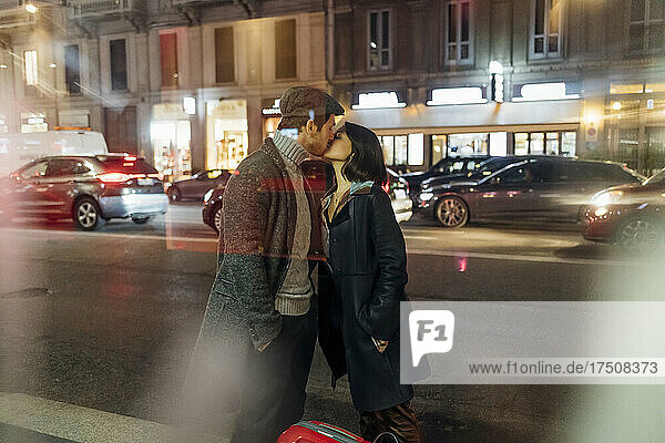 Young couple in warm clothing kissing on illuminated city street