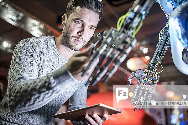 Engineer examining robotic arm holding tablet PC at workshop
