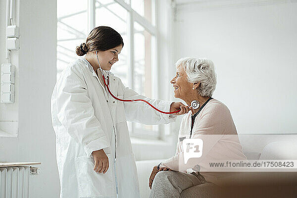 Girl wearing lab coat checking woman with stethoscope at home