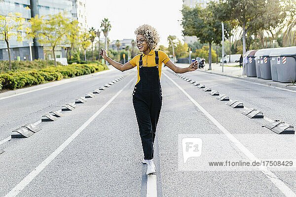 Happy woman with arms outstretched walking on road