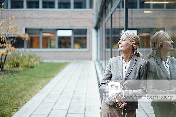 Businesswoman with mobile phone leaning on glass wall