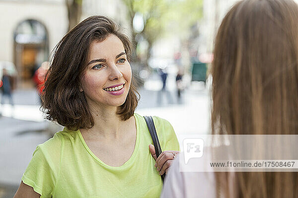 Schöne junge Frau mit kurzen Haaren im Gespräch mit einer Freundin auf dem Fußweg