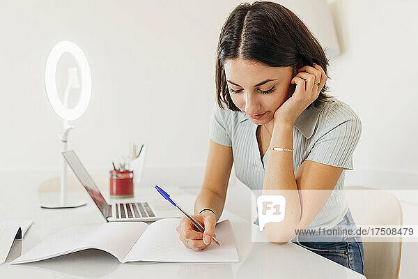 Young businesswoman writing in book on table at home office