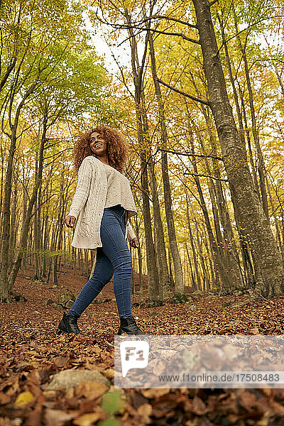 Smiling young woman walking on leaves in autumn forest