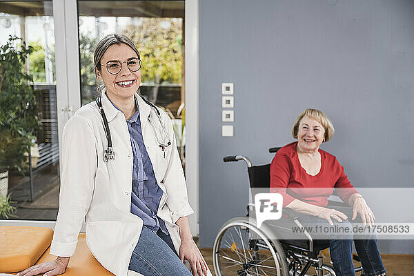 Happy doctor sitting with woman in wheelchair at home