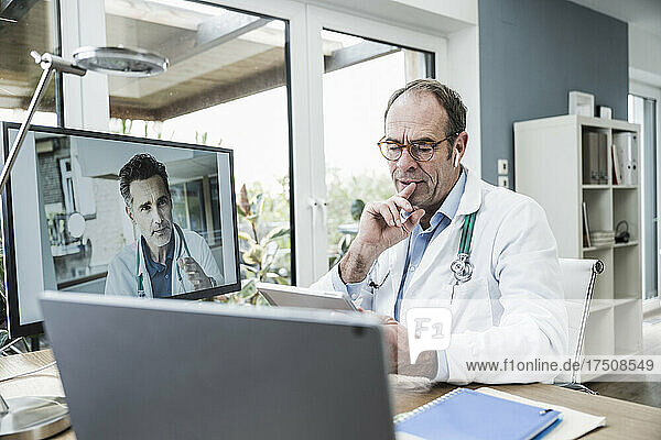Thoughtful doctor with digital tablet on video call with colleague in office