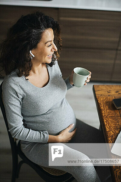 Schwangere Freiberuflerin im Gespräch über Bluetooth bei einem Kaffee zu Hause