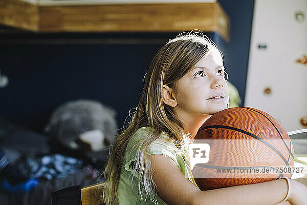 Mädchen schaut nach oben  während sie mit einem Basketball zu Hause sitzt