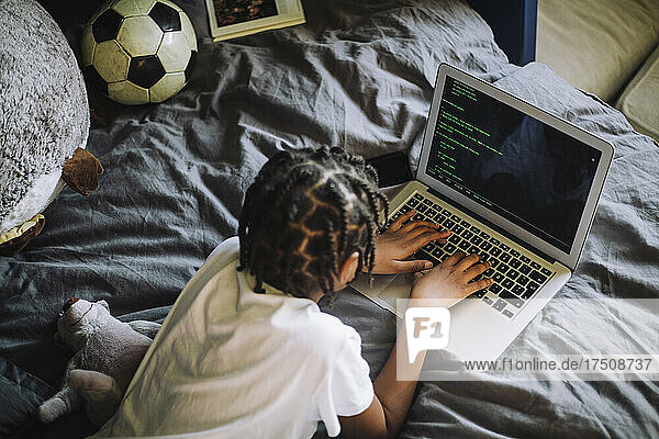 High angle view of girl learning typing on laptop in bedroom