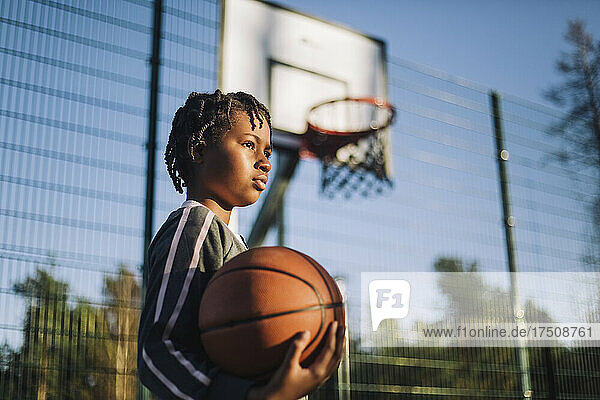 Kontemplatives Mädchen  das an einem sonnigen Tag mit einem Basketball wegschaut