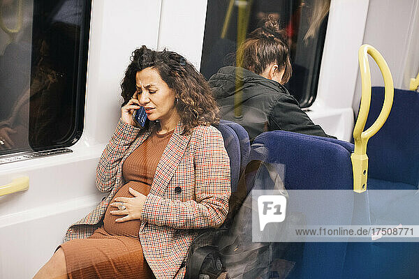 Schwangere Geschäftsfrau  die im Zug sitzend mit ihrem Smartphone telefoniert