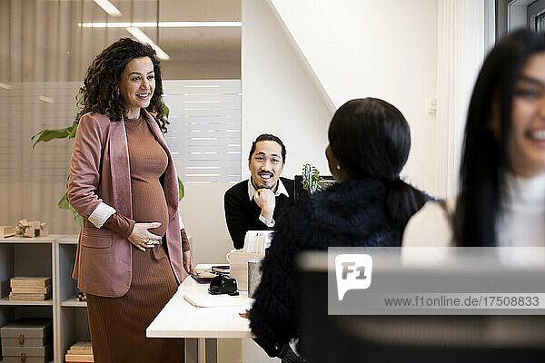 Pregnant businesswoman discussing with male and female colleagues in office
