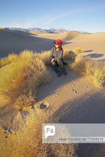 Frau sitzt bei Sonnenaufgang im Sand im Death Valley.