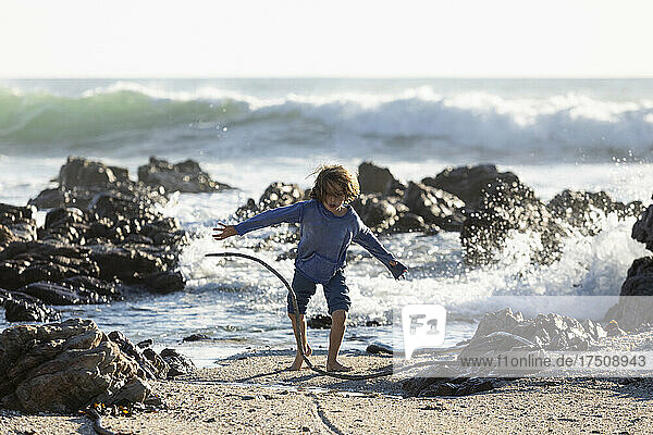 Young boy playing on the sand among rocks on a beach  surf waves breaking