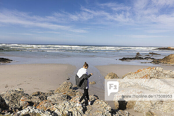 Teenager-Mädchen steht auf Felsen mit Blick auf einen Sandstrand