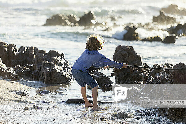 Boy playing on a rocky beach  holding a long kelp seaweed strand