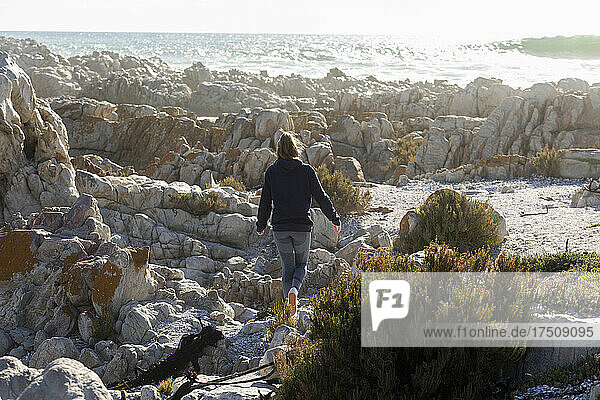Teenage girl climbing on the jagged rocks on a beach  large waves breaking on the shore