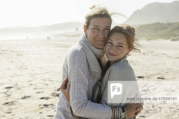 Adult woman and her teenage daughter hugging  standing on a windswept beach