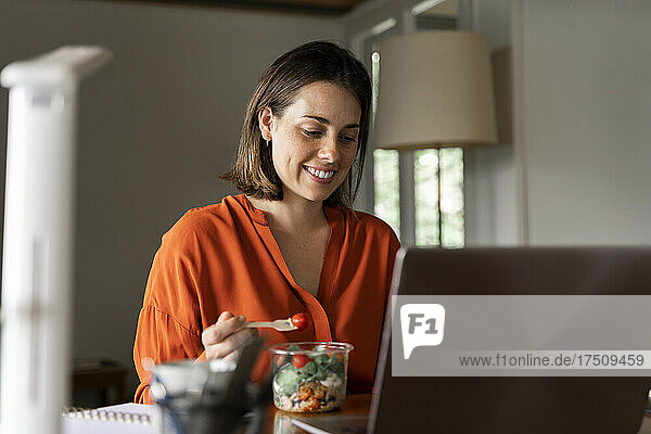 Smiling business person eating salad at home