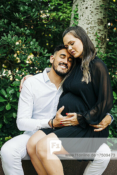 Pregnant woman sitting on lap of smiling man in park