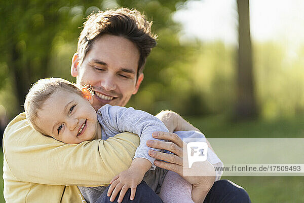 Portrait of happy toddler girl cuddling with her father in a park
