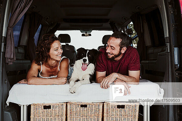 Smiling couple with dog lying in camper trailer