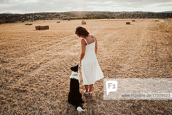 Woman standing by dog in field during sunset