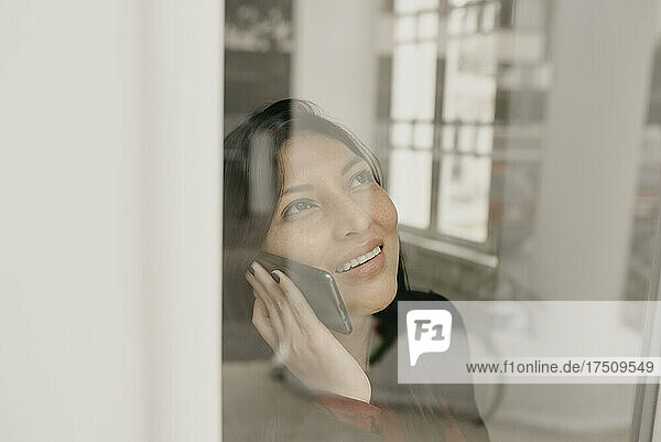 Portrait of smiling woman using smartphone behind window pane