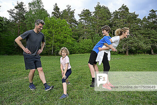 Happy parents exercising with children on grassy land against trees in forest