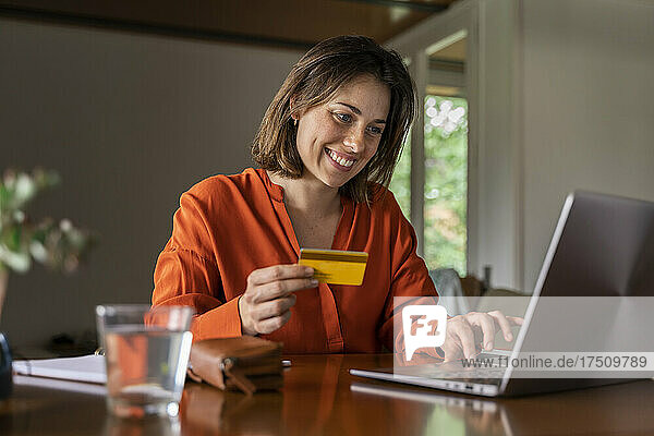 Smiling businesswoman with credit card using laptop at home