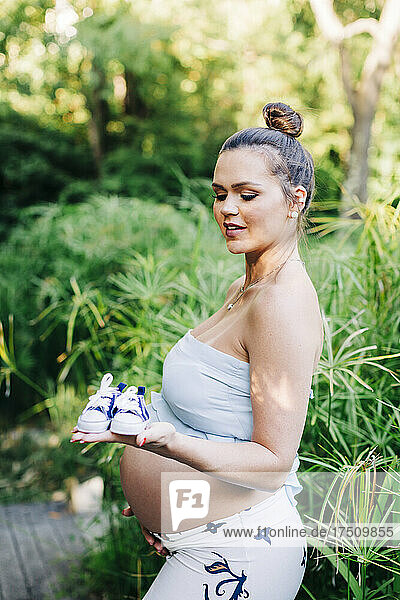 Pregnant woman holding baby booties while standing at public park