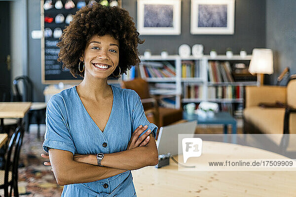 Happy young woman standing arms crossed in modern coffee shop