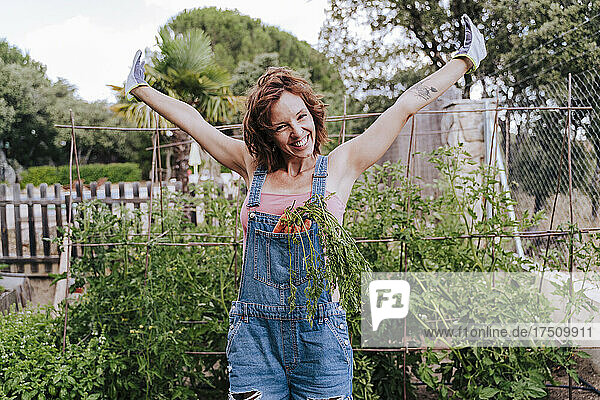 Cheerful woman with arms raised standing against plants in vegetable garden