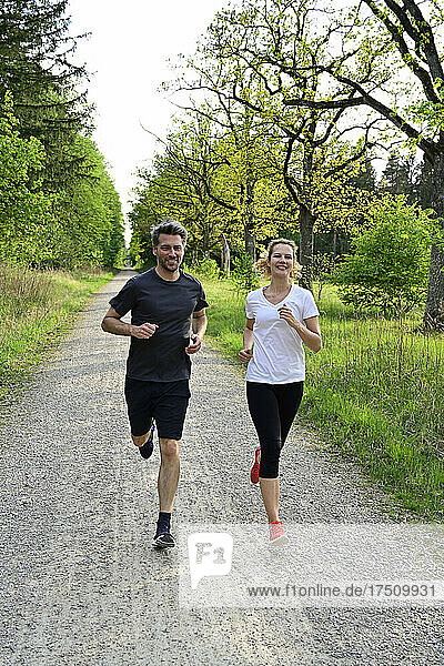 Happy couple jogging on dirt road against trees and plants in forest